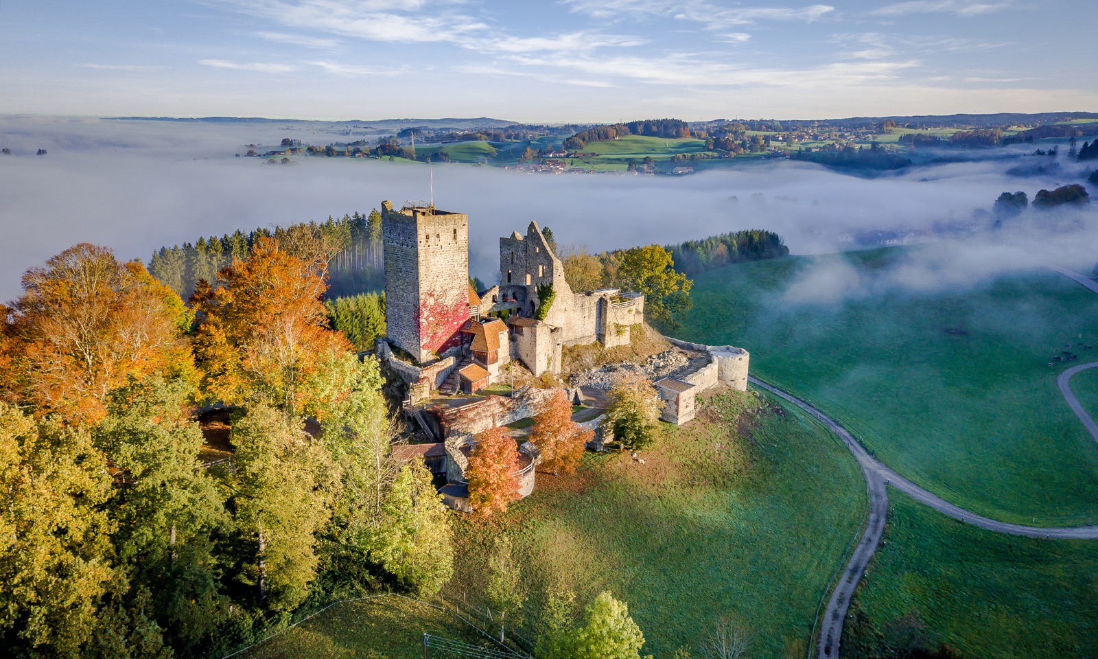 Luftbild der Burgruine Sulzberg im Herbst, dahinter Nebel über dem Allgäu